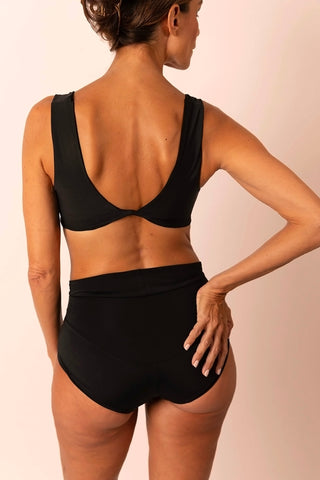 Back view of mature woman wearing a black two-piece bikini set: a swim top with wide straps and center back twist & high-waisted swim bottom
