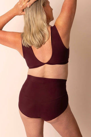 Back view of larger mature woman wearing a burgundy two-piece bikini set: a swim top with wide straps and center back twist & high-waisted swim bottom