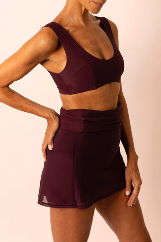 Side view of mature woman wearing a burgundy swim top and matching high-waist swim skirt skort