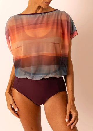 Mature woman wearing a one piece swimsuit with flowy sunset striped top & solid burgundy bottom