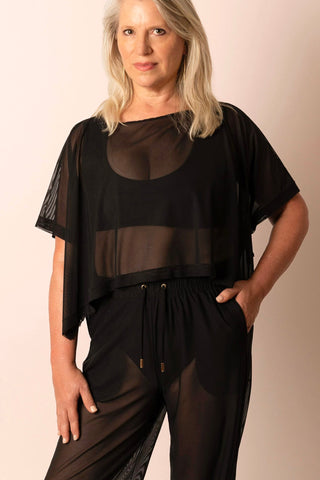 Mature woman wearing a black top and pants with sheer panels on a beige background
