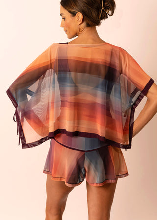 Back view of mature woman wearing a sheer flowy sunset striped top and matching swimsuit