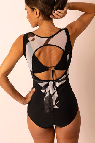 Back view of mature woman wearing a black and white geometric printed tie top one piece swimsuit with matching custom swim top