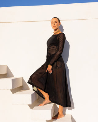 Woman in a sheer black dress standing on white steps with a blue sky background