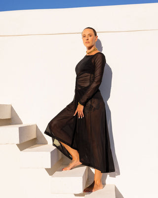 Woman in a sheer black dress standing on white steps with a blue sky background