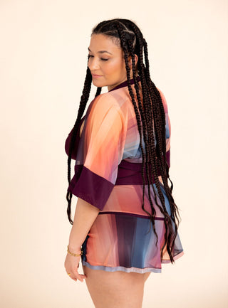 Woman wearing a colorful swim outfit with sheer sleeves and a patterned skirt against a beige background