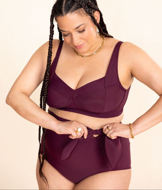 Woman wearing a maroon swimsuit with a beige background