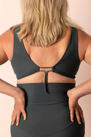 Back view of woman wearing blue-grey bikini on plain background