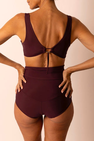 back view of woman wearing a burgundy swimsuit with a plain background