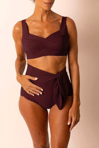 Woman wearing a burgundy swimsuit with a plain background