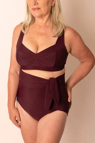 Woman wearing a burgundy swimsuit against a beige background